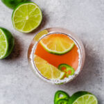 A glass of grapefruit margarita with limes and jalapeños