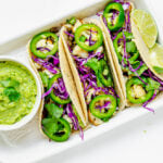 A plate of tacos featuring a lentil and cauliflower filling, topped with guacamole, red cabbage and jalapeños.