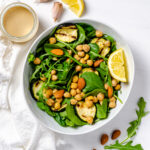 A bowl of spinach arugula zucchini, almond and chickpea salad with a garlic tahini dressing