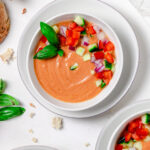 A bowl of gazpacho garnished with basil, peppers, cucumbers, red onion