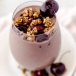 Close up of a glass of a chocolate-cherry smoothie with cherries and granola.