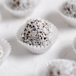 Close up photo of a vegan dark chocolate truffle coated with coconut flakes in a wrapper