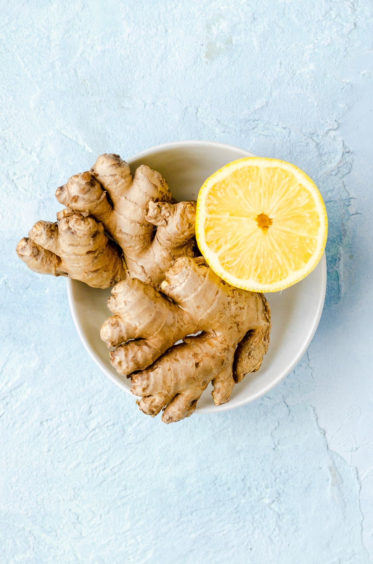 Close up of a bowl with ginger and half a lemon.