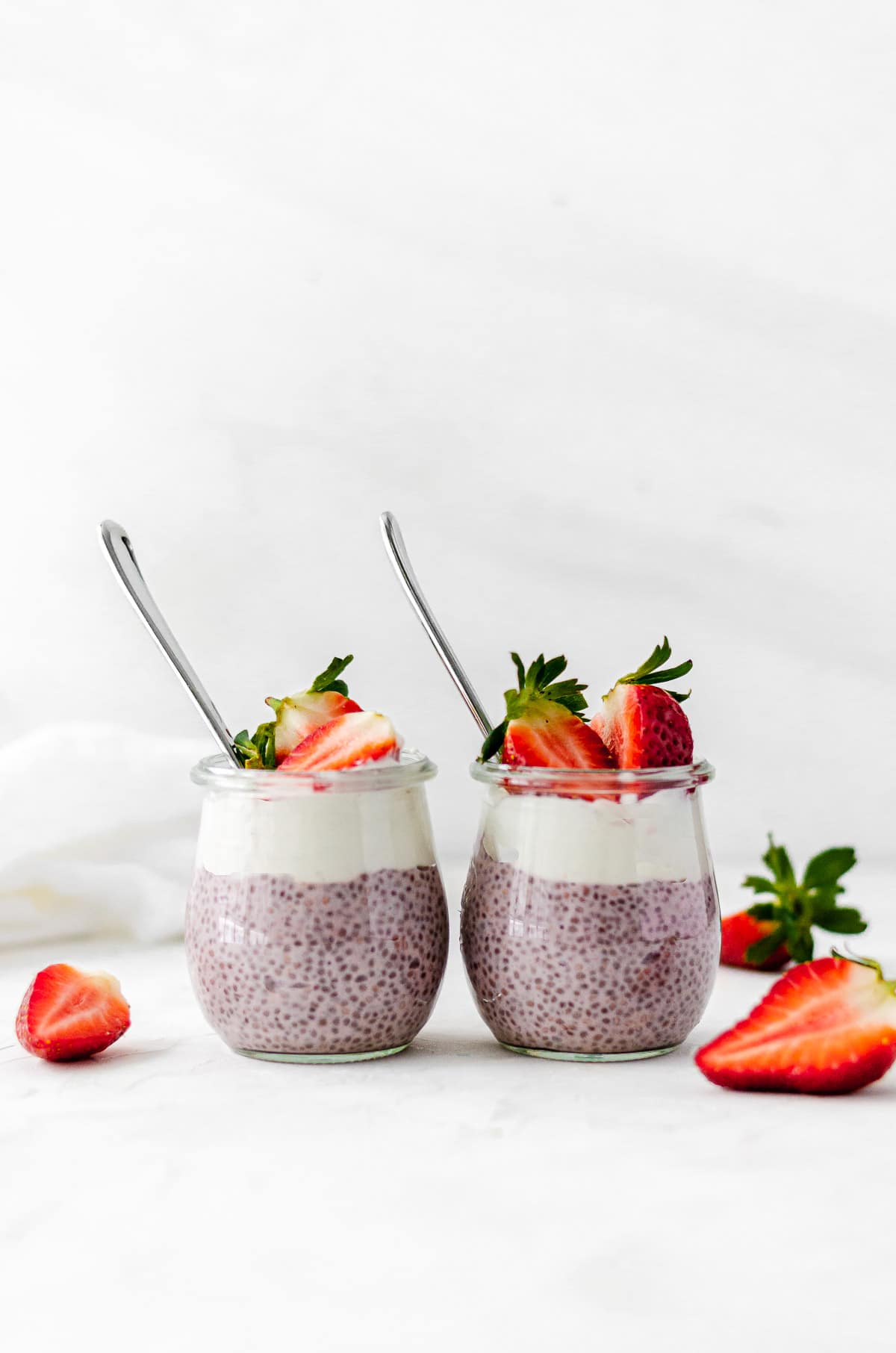 Two jars of strawberry chia seed pudding side by side with a layer of coconut yogurt and topped with strawberries.