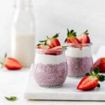 Two small jars of pink strawberry chia seed pudding with a layer of coconut yogurt topped with strawberries.