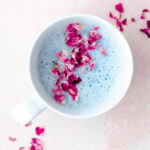 A cup of blue lavender moon milk decorated with rose petals.