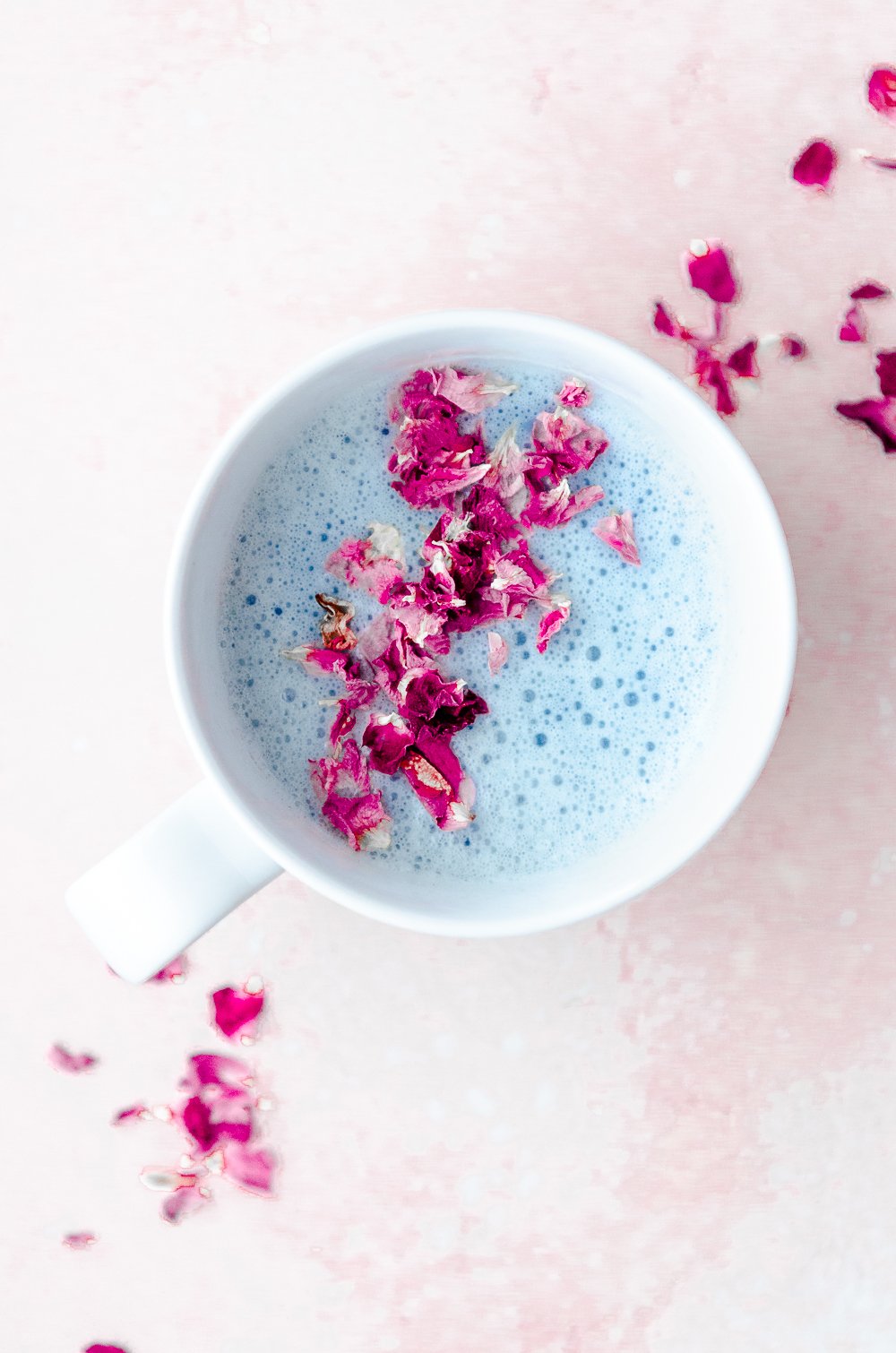 A cup of blue lavender moon milk decorated with rose petals.