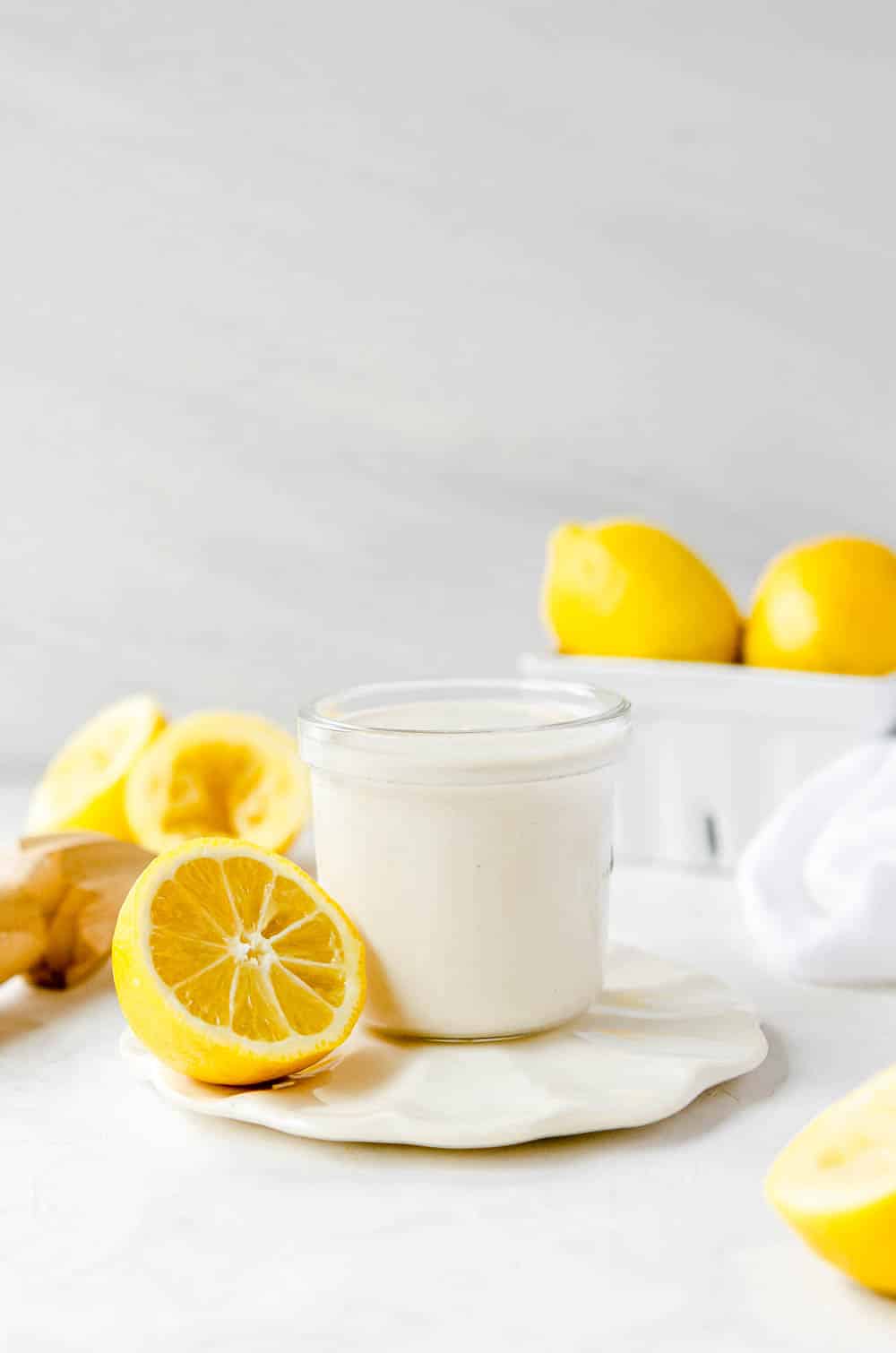 Small glass jar of oil-free tahini dressing on a small coaster surrounded by lemons. 