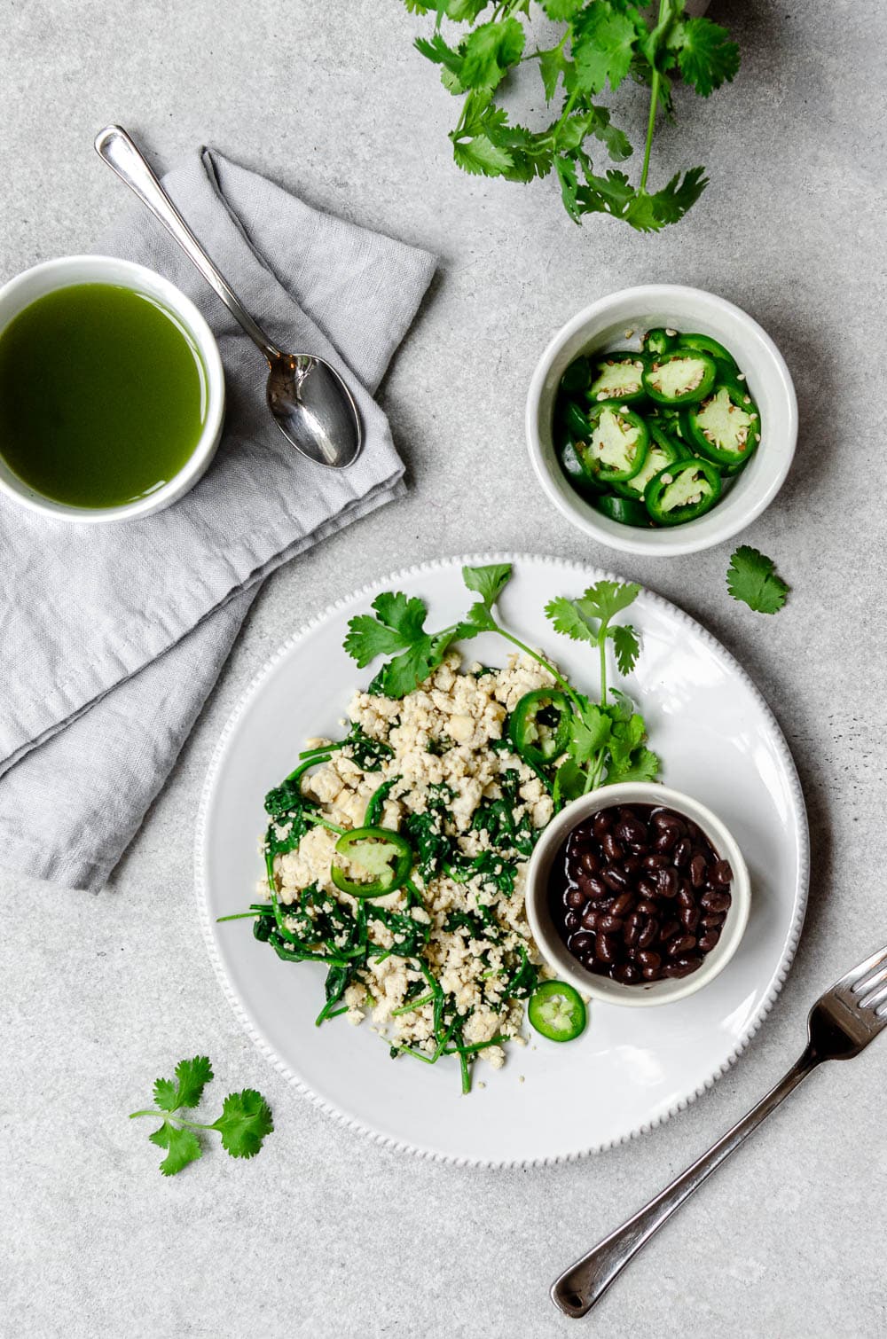 Plate with vegan tofu scramble, spinach, cilantro, jalapeño with a side of black beans and green tea.