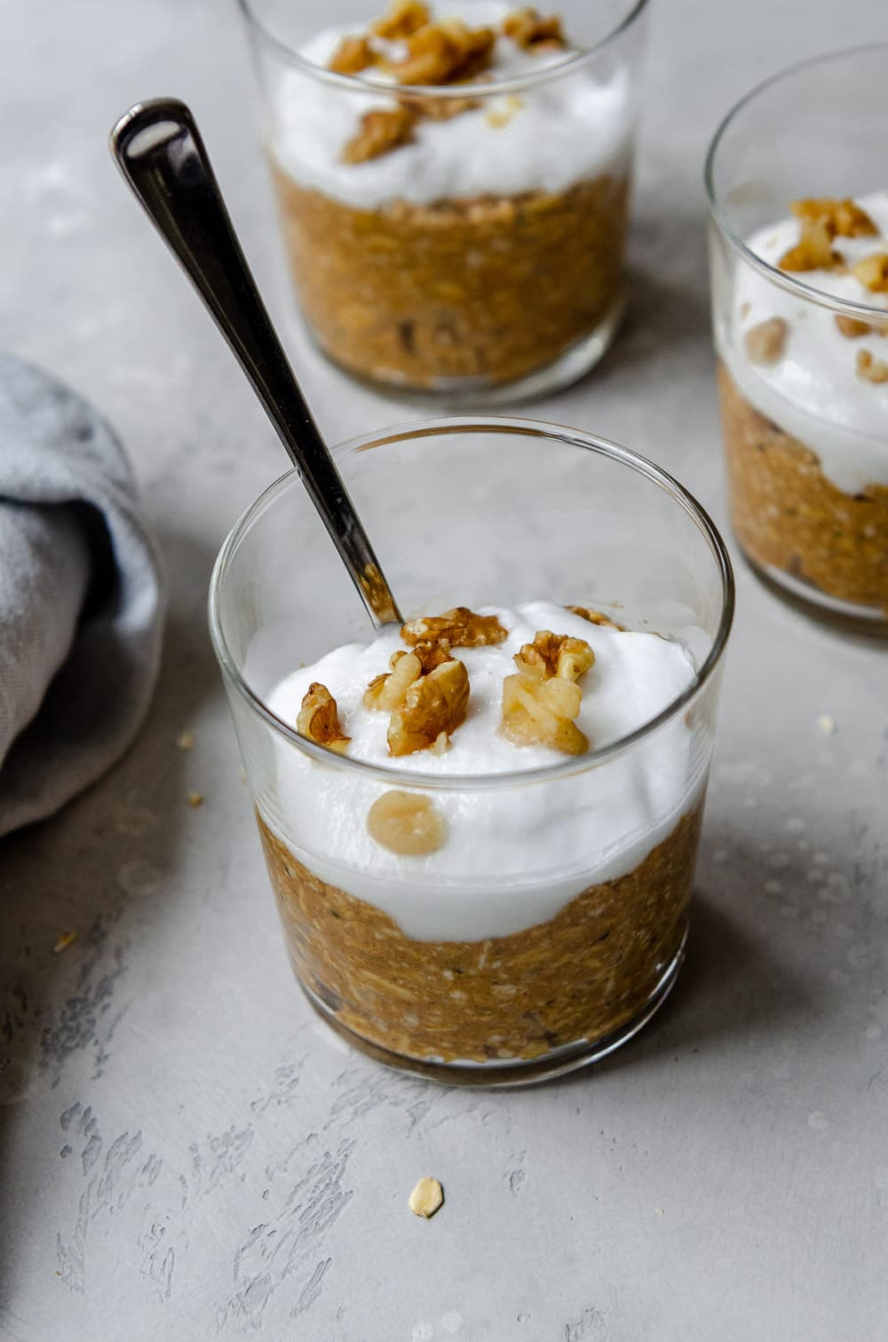 Three jars of vegan, pumpkin spice overnight oats topped with coconut yogurt and walnuts.