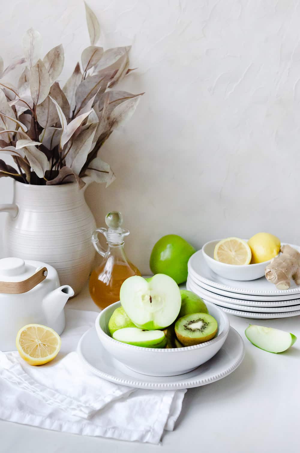 Reduce bloating with apple cider vinegar, green apples, lemons, kiwi arranged on plates with ginger tea.