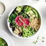 Close up of a quinoa bowl with roasted broccoli, eggplant, edamame, baby spinach, advocacy and garnished with purple radish and broccoli sprouts