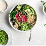 Bowl with roasted broccoli, eggplant, edamame, quinoa, baby spinach and garnished with broccoli spouts and avocado.