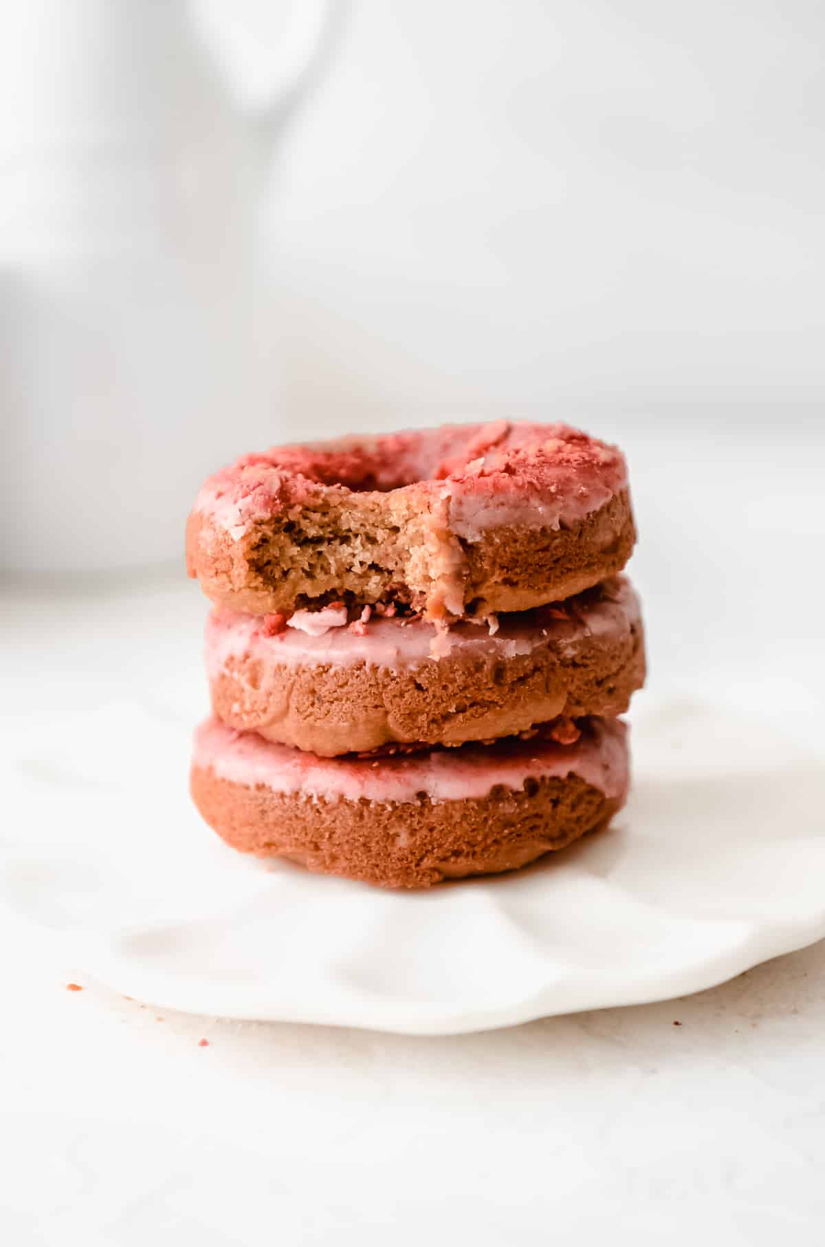 Stack of three baked strawberry donuts on a plate with a bite taken out of one of them.