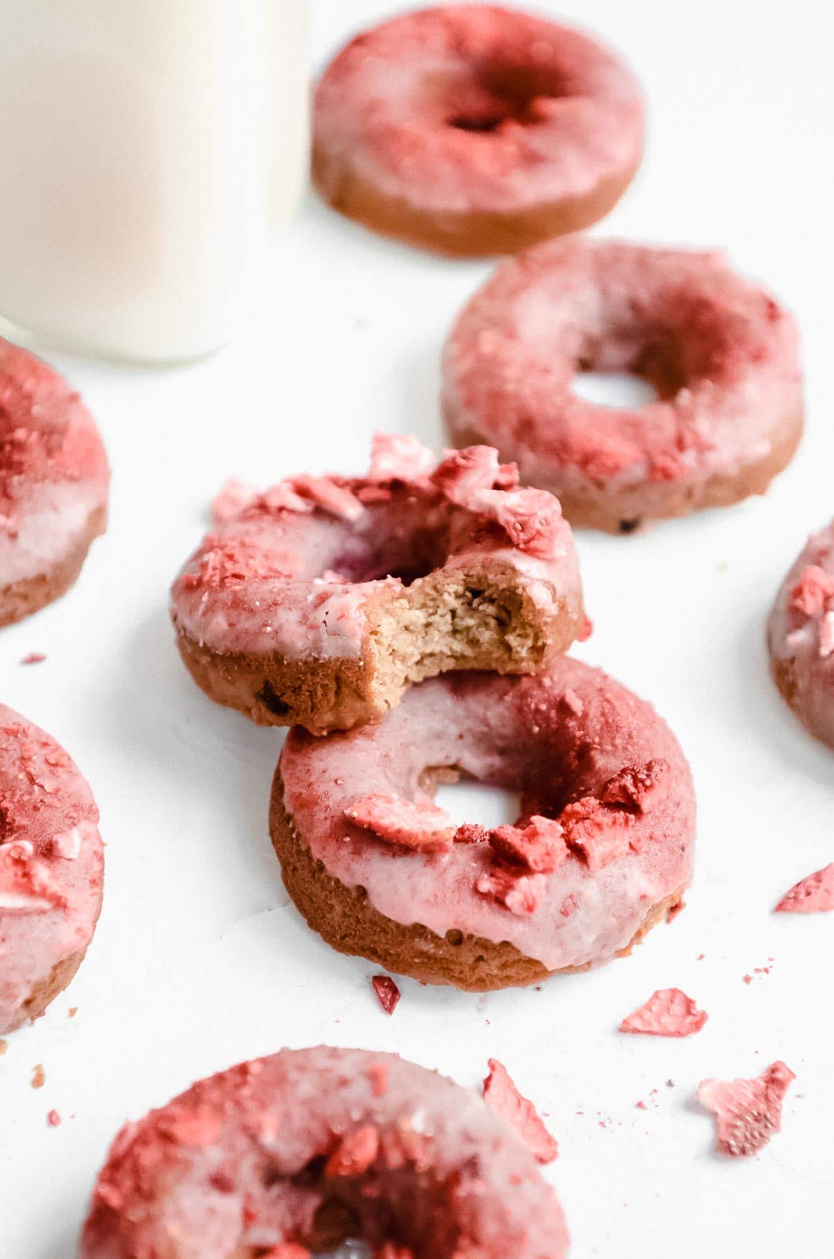 Seven baked strawberry donuts arranged with a bit taken out of one of the donuts.