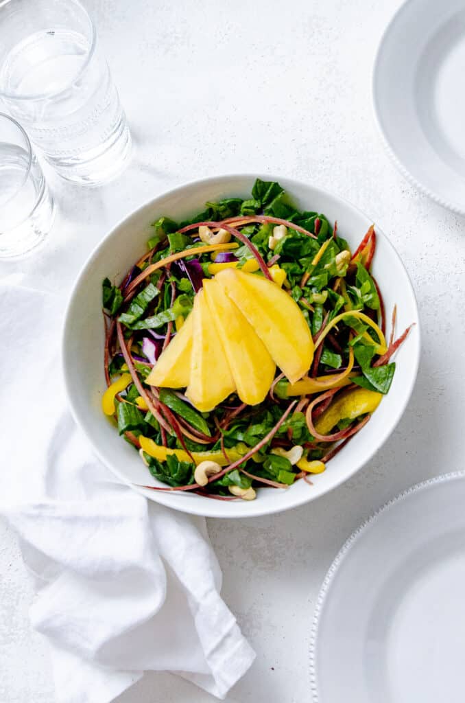 Thai salad with peanut dressing - mixed in a bowl with mango, romaine lettuce, yellow pepper, cashews, purple carrot, scallions