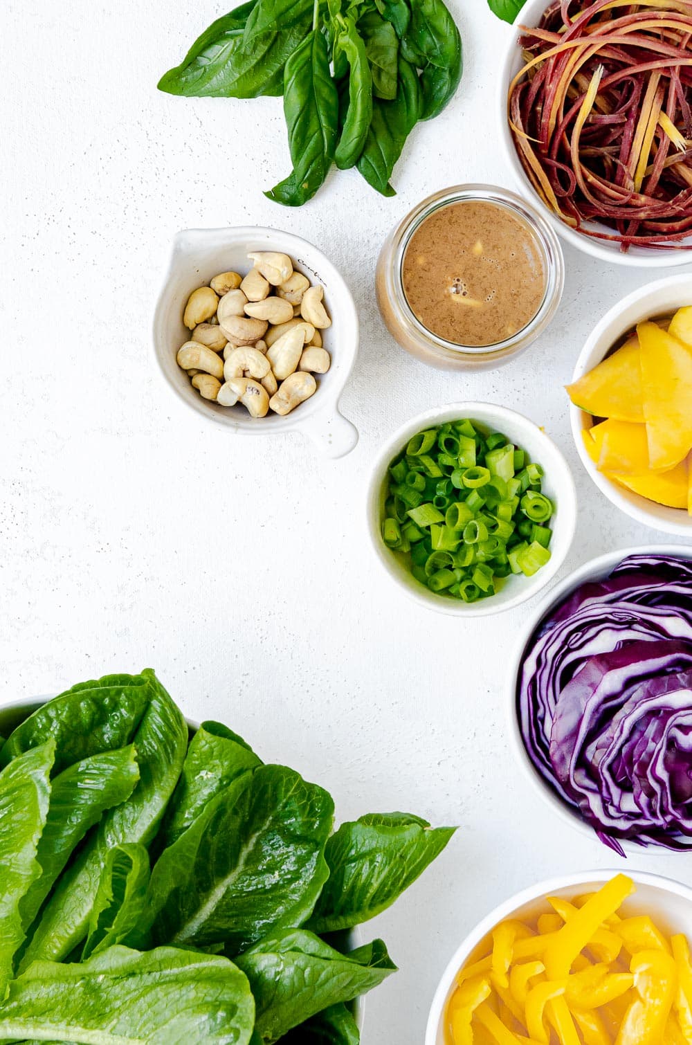 Thai salad ingredients - romaine lettuce, yellow bell pepper, red cabbage, green onions, peanut dressing, mango, carrots and cashews