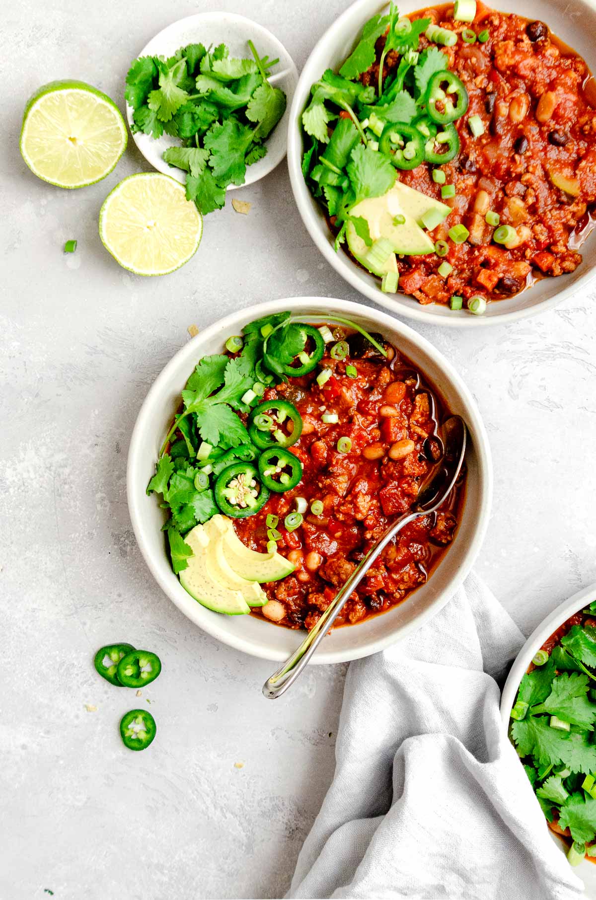 Two bowls of turkey vegetable chili garnished with jalapeño, cilantro, scallions and avocado. 