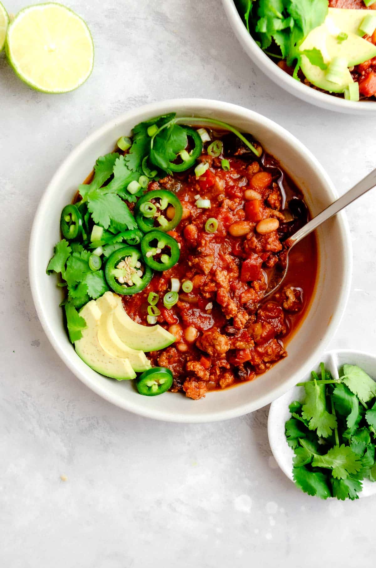 Close up of a bowl of turkey vegetable chili garnished with jalapeño, cilantro, scallions and avocado. 