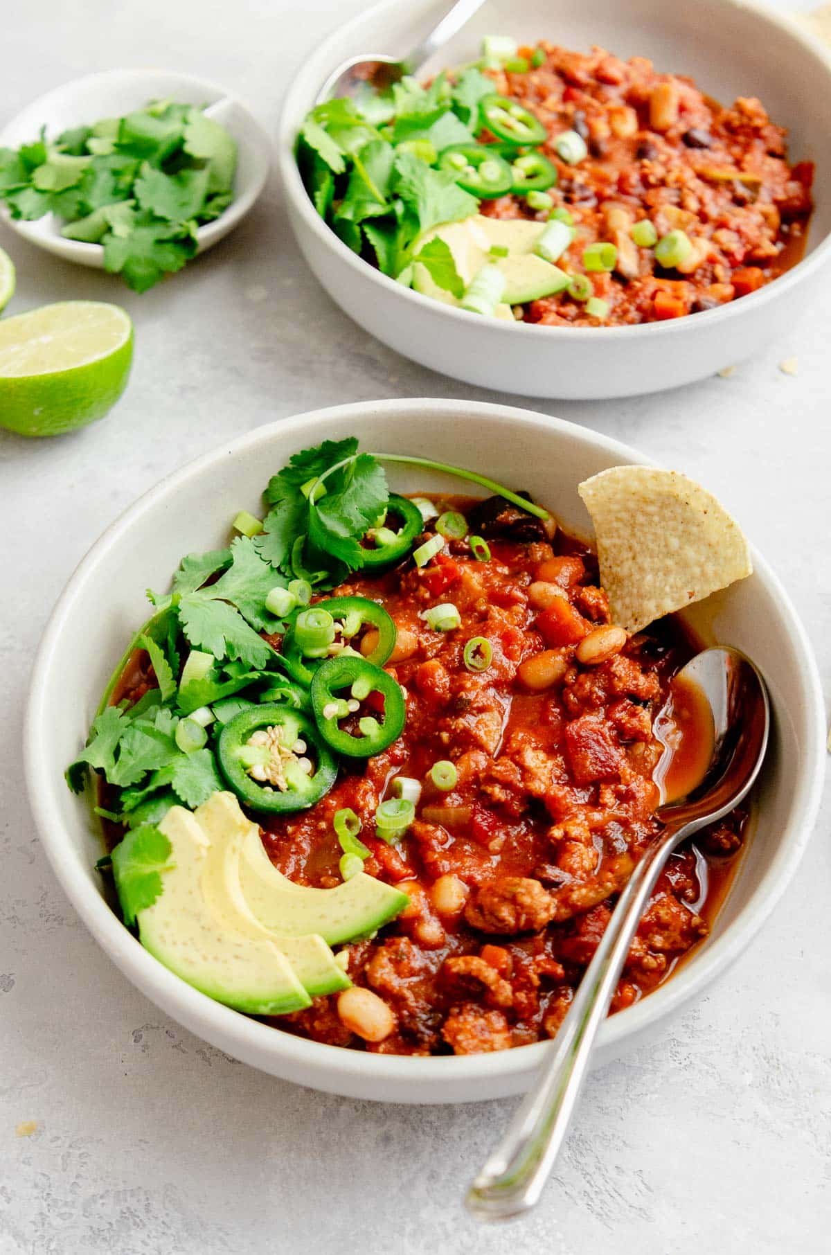 Bowl of healthy turkey vegetable chili garnished with scallions, jalapeño, cilantro, avocado and tortilla chips. 