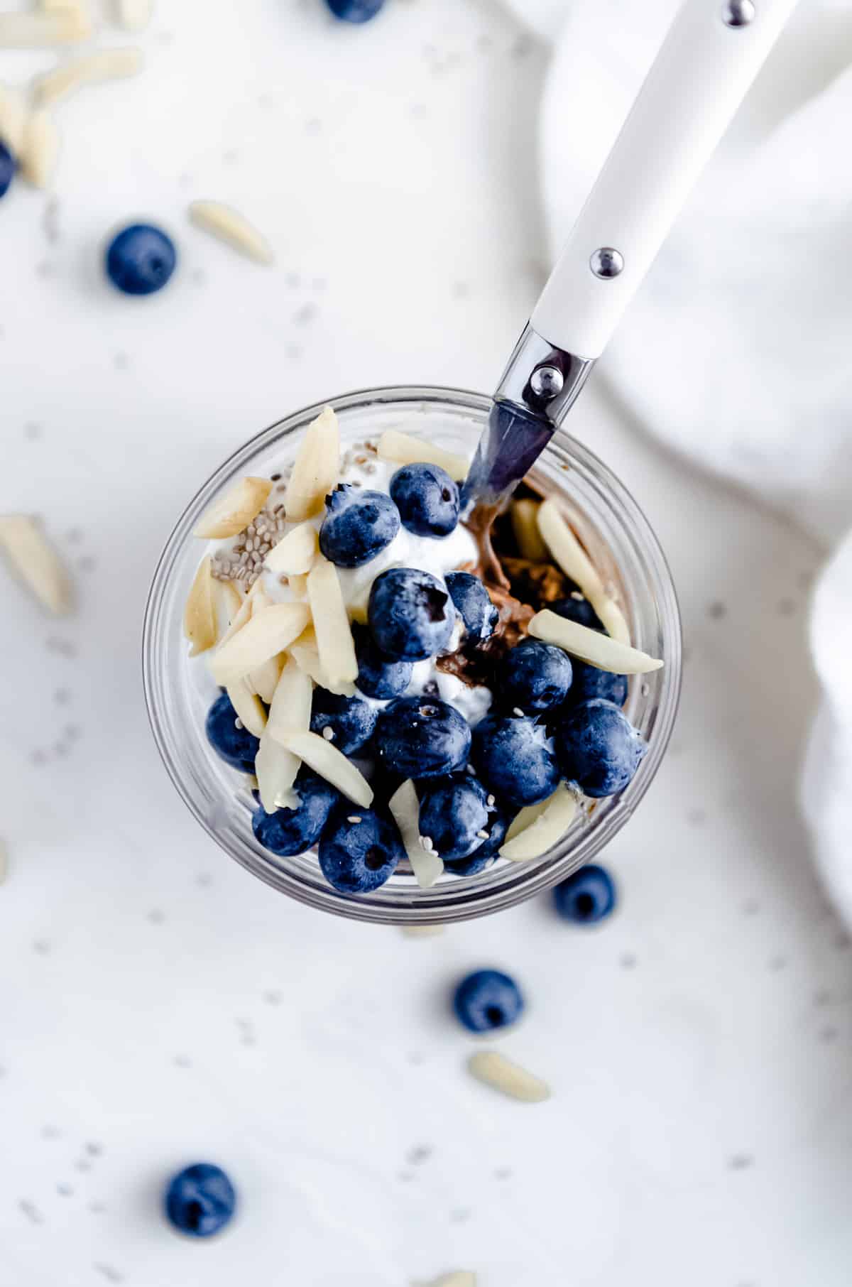 Close up overhead photos of chocolate overnight oats with almond butter garnished with blueberries, almond slivers and chia seeds with a spoon peeking out of the jar.