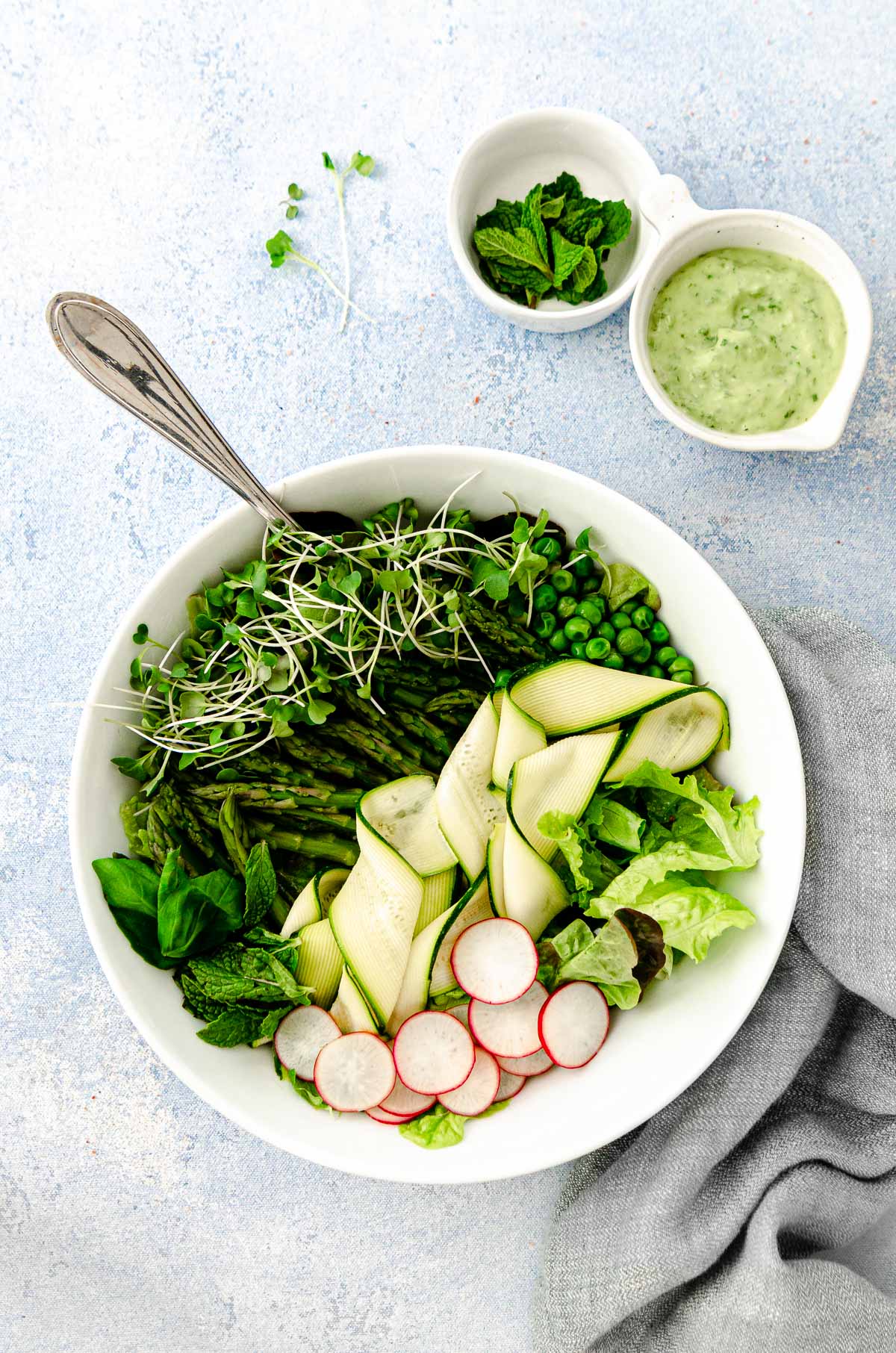 Green goddess salad with butter lettuce, radishes, mint, asparagus, peas, zucchini ribbons with a small dish of vegan avocado green goddess dressing a mint.