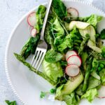 Close up of green goddess salad with asparagus, radishes, mint, zucchini, peas and butter lettuce with a fork with an asparagus spear.