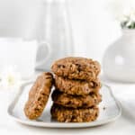 Four banana oatmeal breakfast cookies stacked on a small white plate with one cookie leaning against the stack.