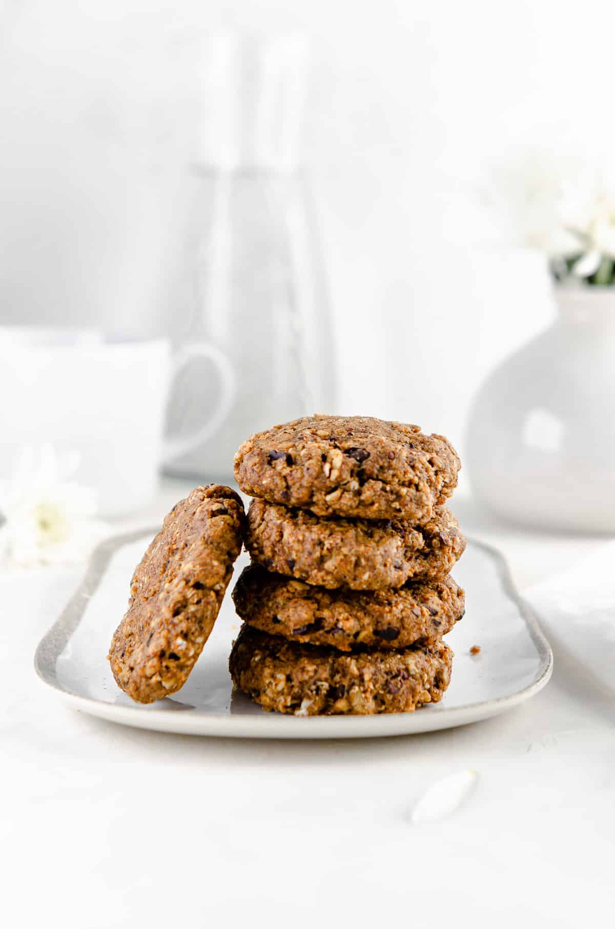 Four banana oatmeal breakfast cookies stacked on a small white plate with one cookie leaning against the stack.