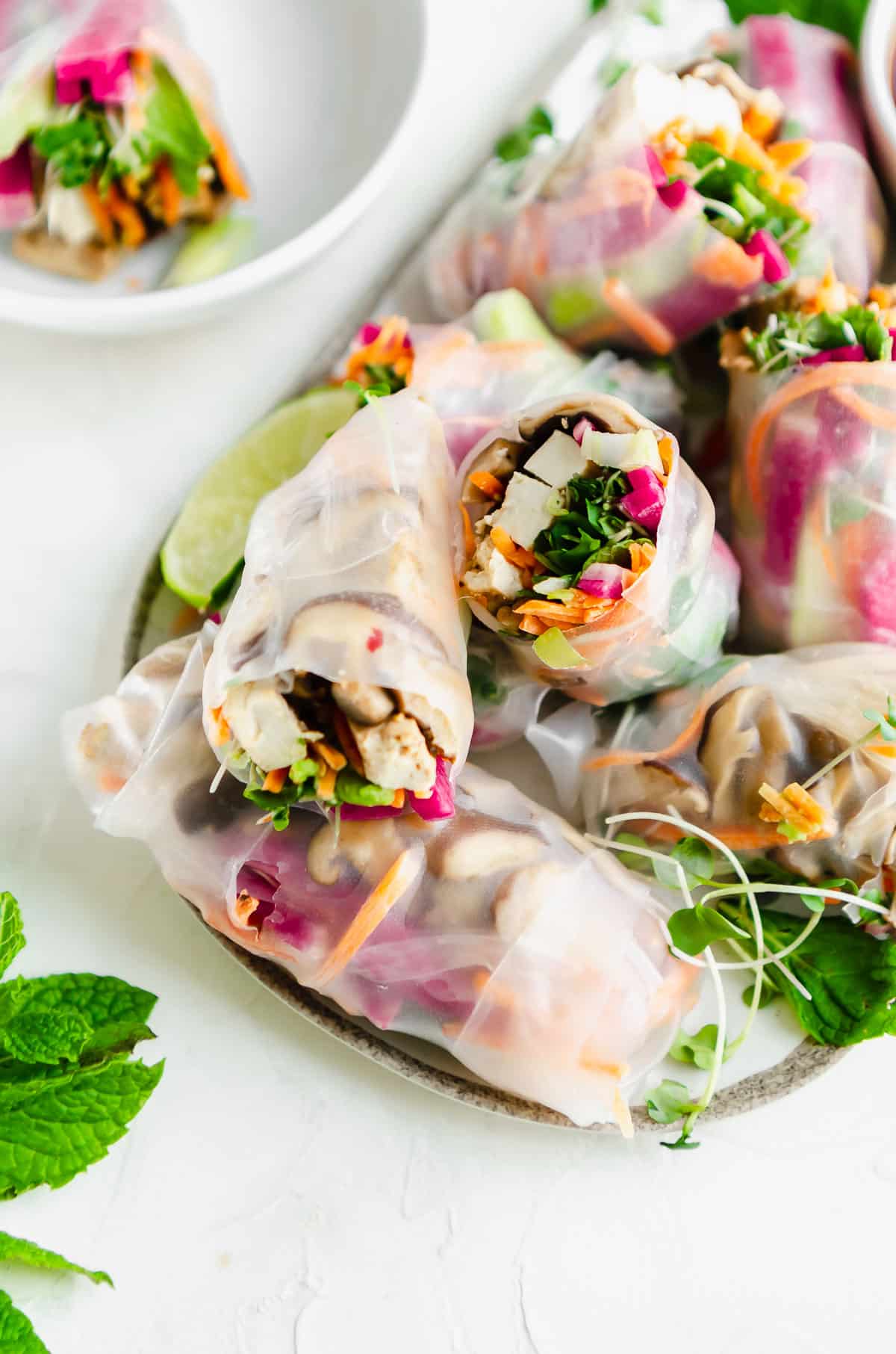 Tofu summer rolls on a plate filled with shiitake mushrooms, carrots, watermelon radish, scallions, mint, microgreens and avocado