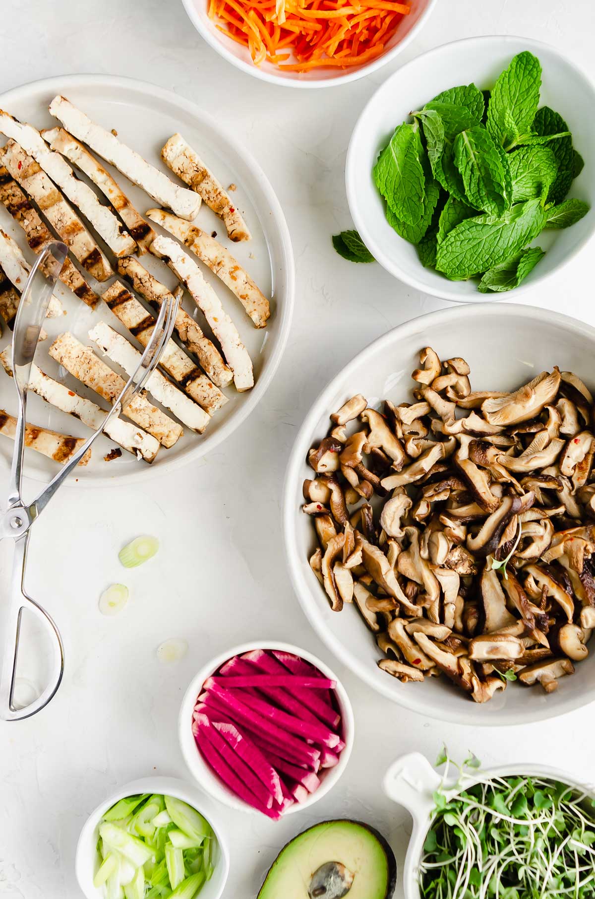 Ingredients for tofu summer rolls which include microgreens, avocado, scallions, watermelon radish, shiitake mushrooms, tofu, mint and carrot