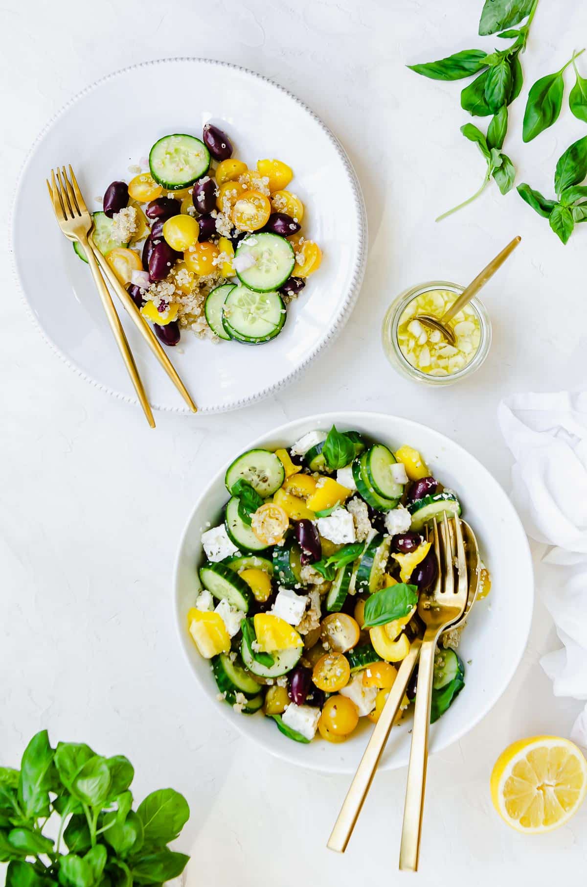 Serving bowl with a Mediterranean Cucumber Tomato salad with cucumbers, yellow tomatoes, kalamata olives, feta, basil, yellow pepper and quinoa, with a lemon dressing.