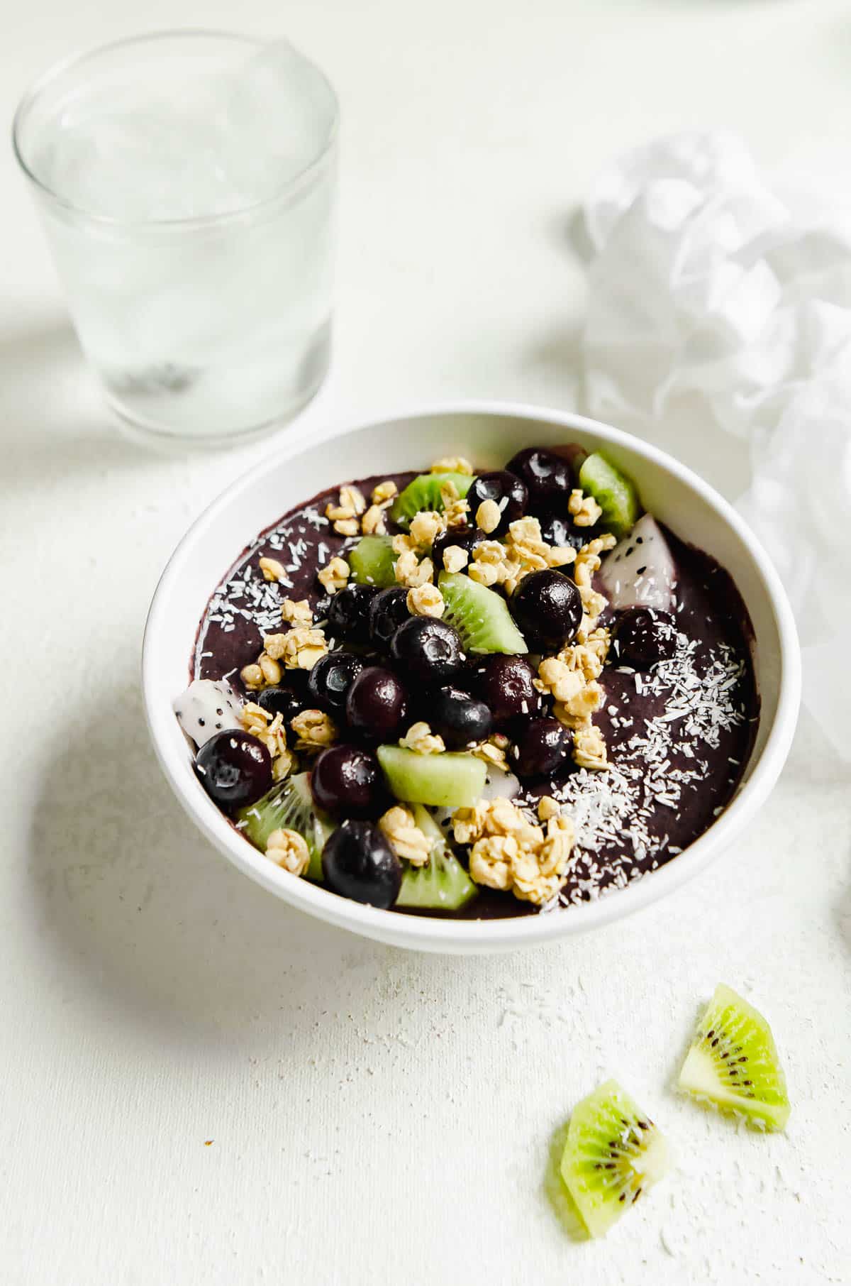 Superfood açaí bowl topped with kiwi slices, dragonfruit, granola, blueberries, with a glass of water