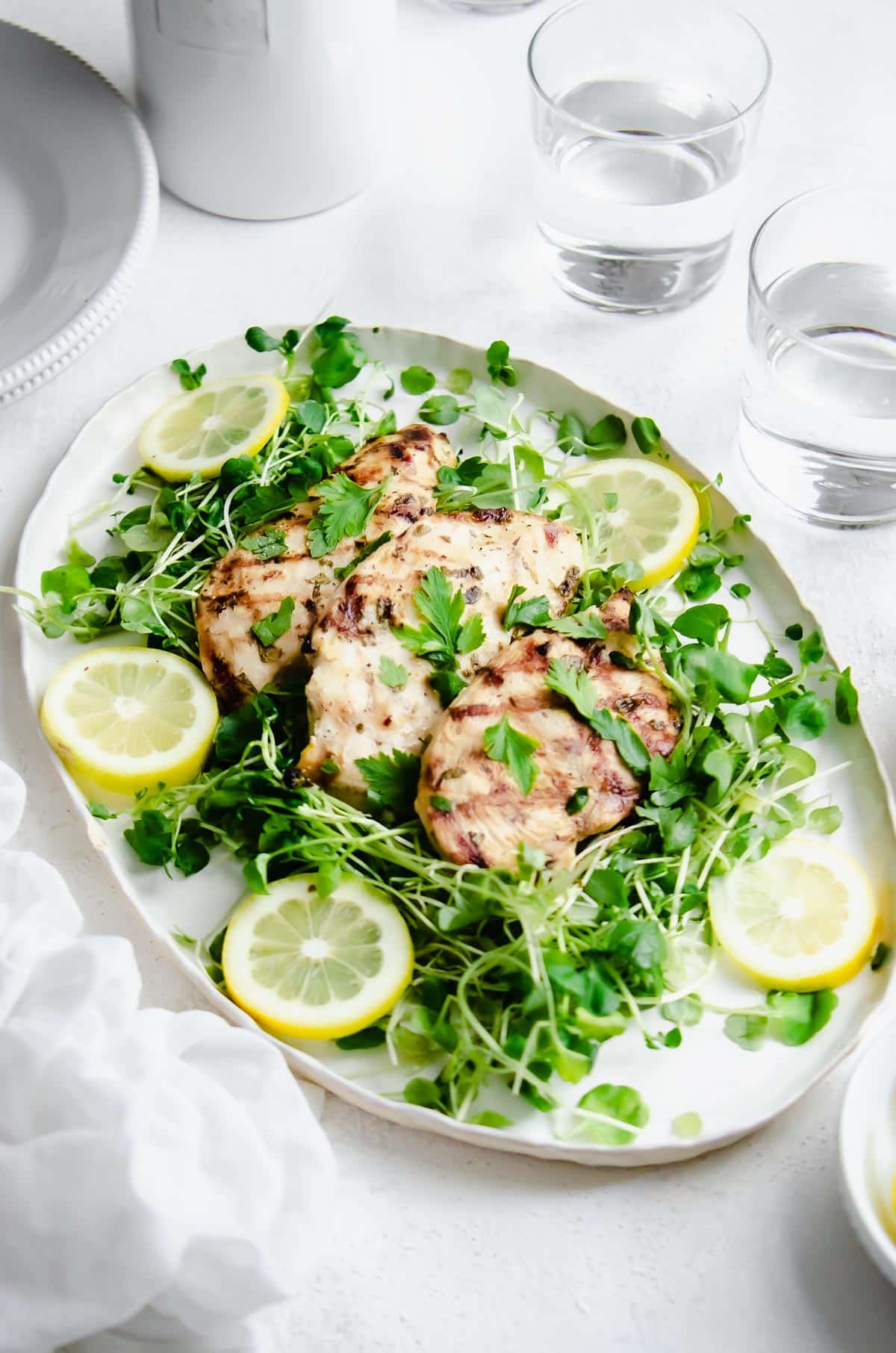 Platter of grilled chicken breast over a bed of greens and garnished with lemons