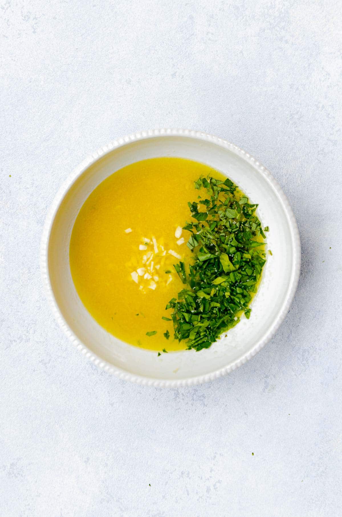 Bowl of greek chicken marinade which includes olive oil, garlic, parsley, lemon juice and oregano