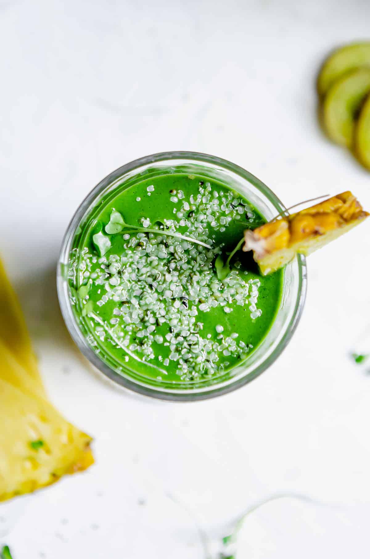 Close up overhead shot of super green tropical smoothie garnished with hemp seeds and a pineapple wedge.