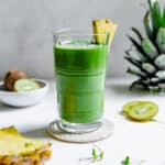 Green smoothie made with banana, pineapple, kiwi, baby spinach, micro greens, hemp seed and spirulina and garnished with a pineapple slice.