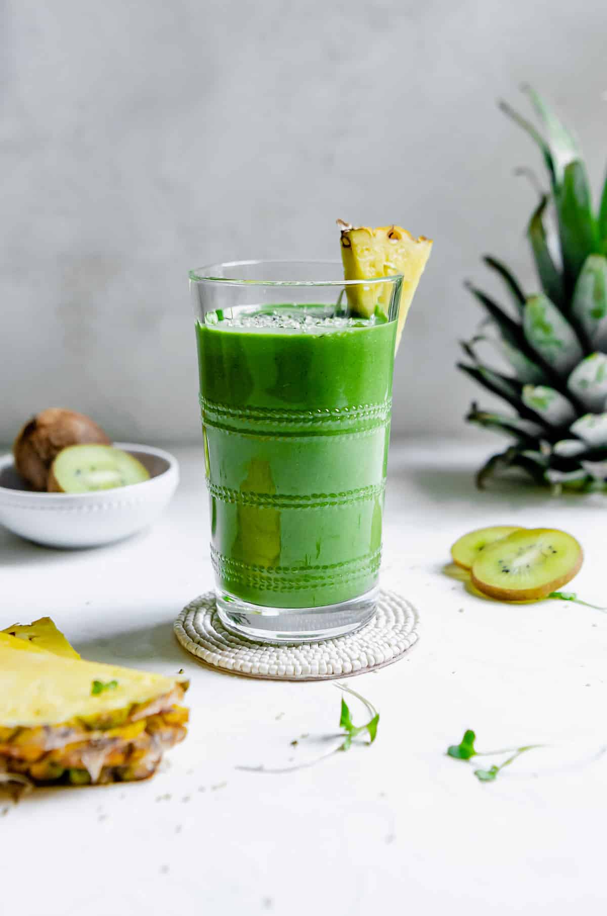 Green smoothie made with banana, pineapple, kiwi, baby spinach, micro greens, hemp seed and spirulina and garnished with a pineapple slice.