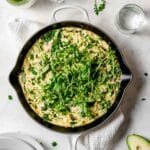 Easy, healthy vegetable frittata in a cast iron pan made with asparagus, leeks, baby spinach, onions and shiitake mushrooms, served with green onions and avocado.