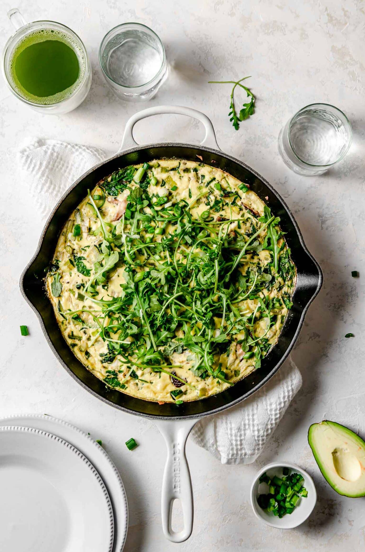 Easy, healthy green vegetable frittata in a cast iron pan made with asparagus, leeks, baby spinach, onions and shiitake mushrooms, served with green onions and avocado.