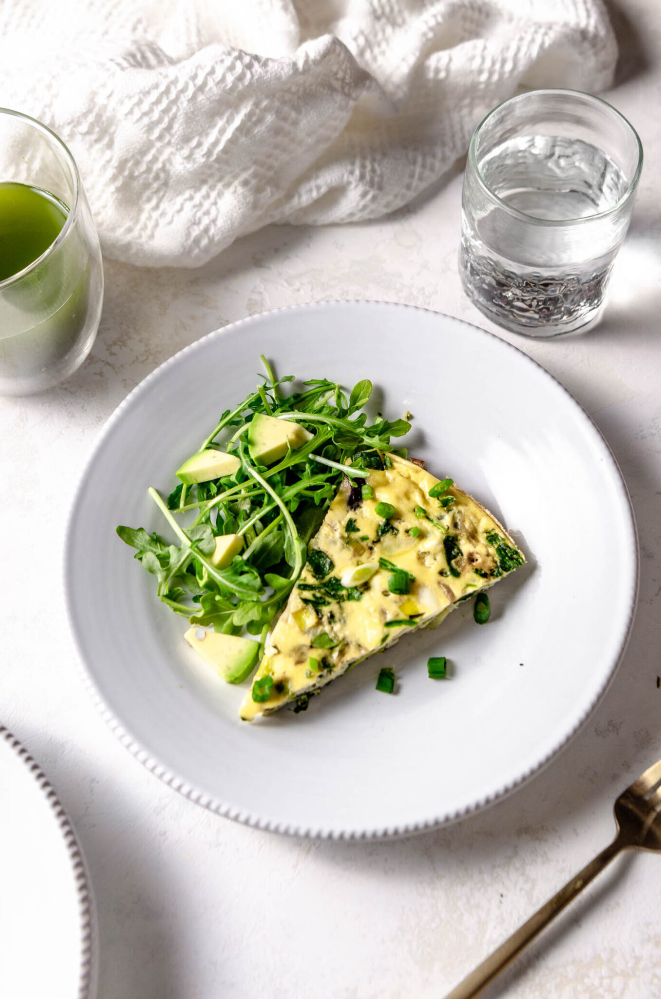 Slice of a green vegetable frittata served with avocado slides and arugula.