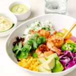 Close up of shrimp burrito bowl garnished with cilantro lime rice, black beans, red cabbage, avocado, and an onion and pepper mixture.