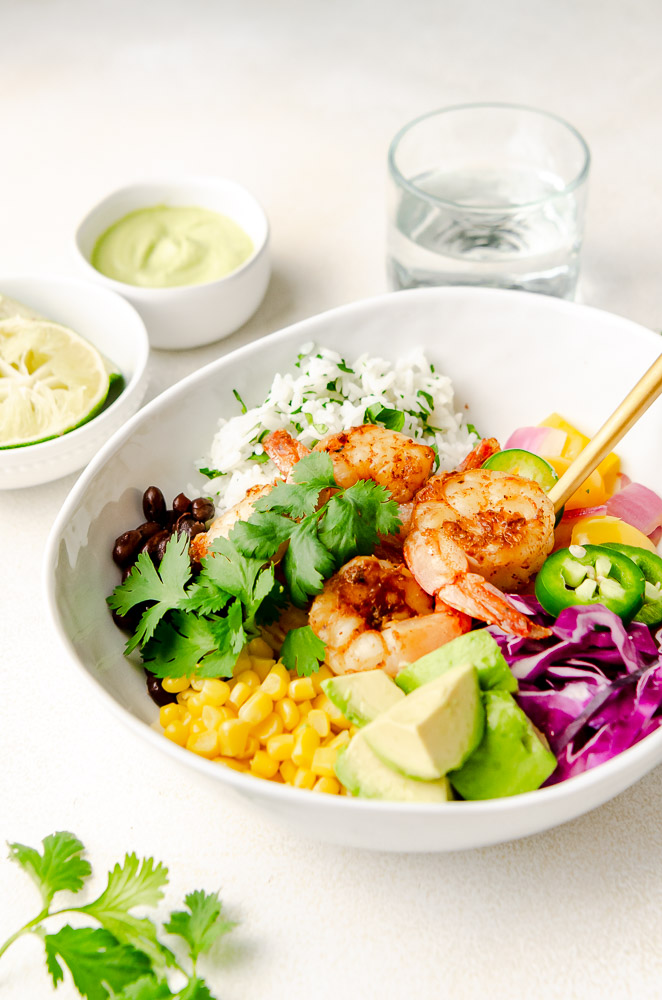 Close up of shrimp burrito bowl garnished with cilantro lime rice, black beans, red cabbage, avocado, and an onion and pepper mixture.