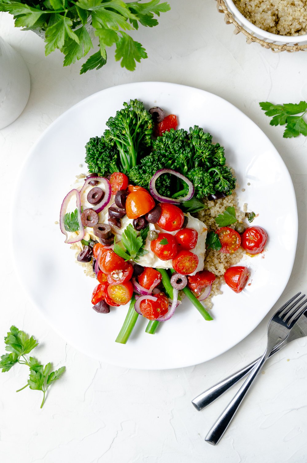 Plate of halibut over quinoa and broccoli topped with a tomato-olive-garlic-caper mixture and parsley. 