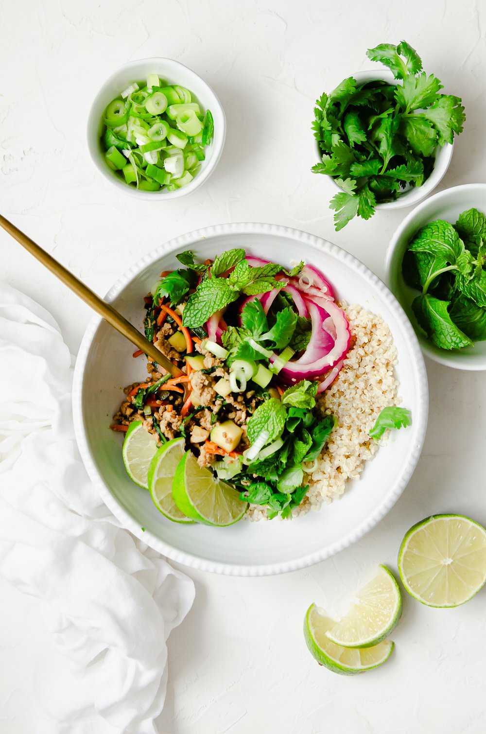 Ground chicken larb bowl made with ground chicken, baby spinach, carrots and zucchini, topped with green onions, cilantro, pickled onions and served with quinoa and limes. 