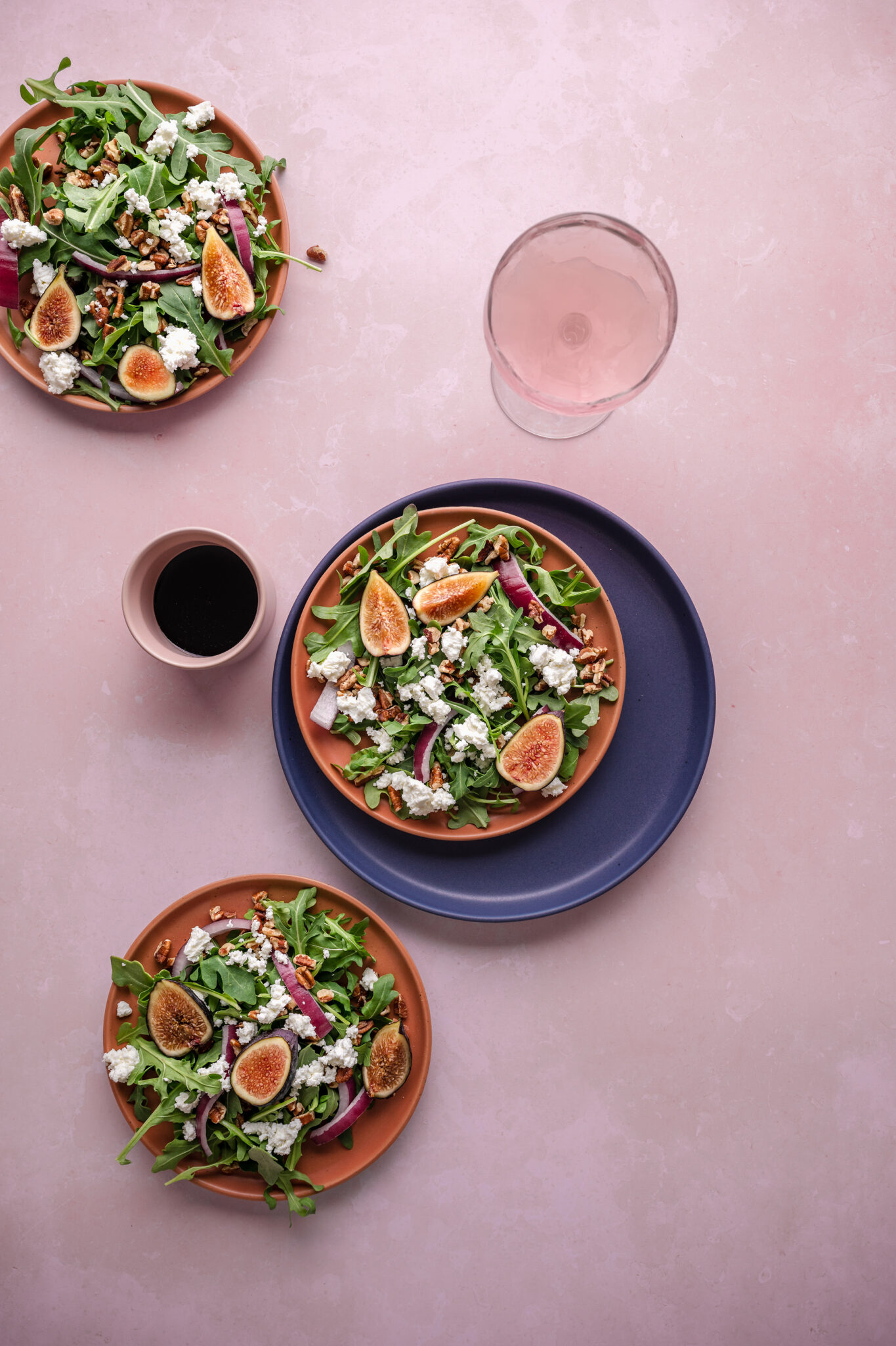 Arugula salad with figs, pecans, red onion and goat cheese on salmon-colored plates; greens and fiber rich fruits support gut health which support hormone balance.