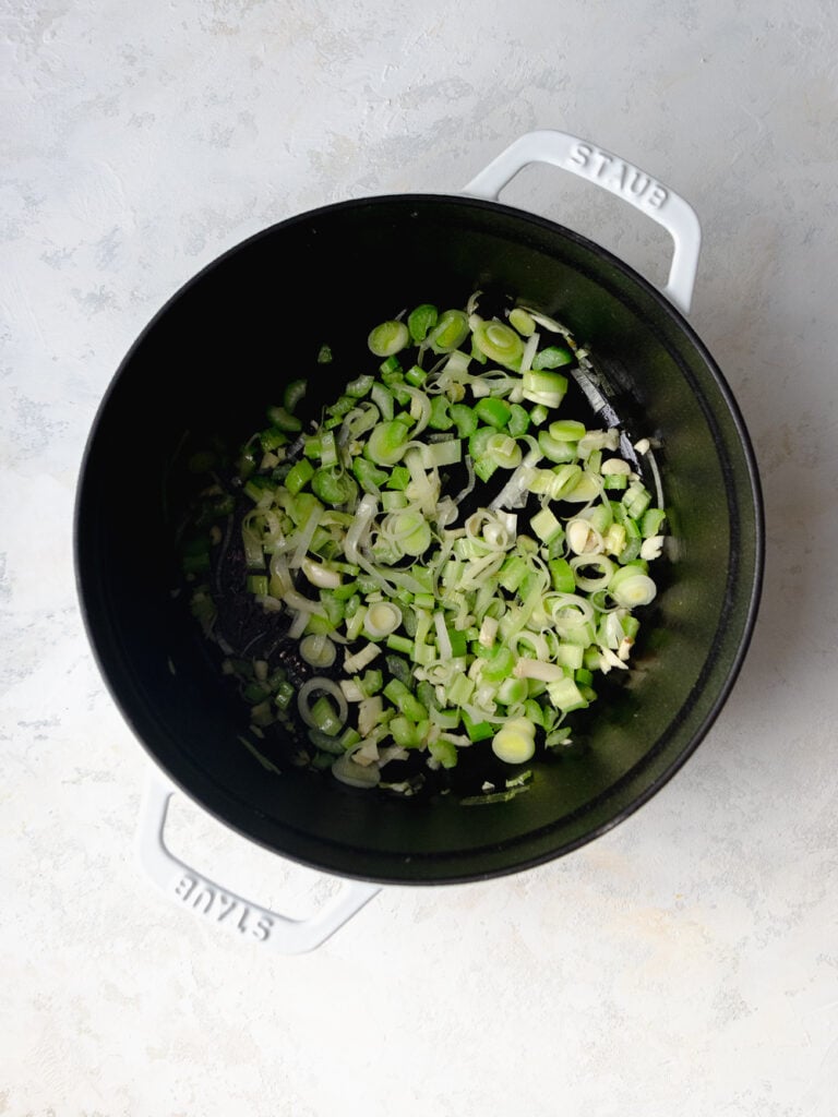 White Staub cast iron pot with sautéed leeks and celery.