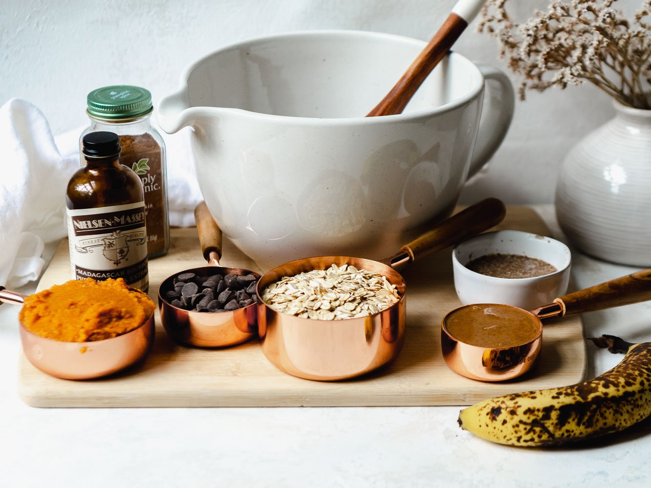 Ingredients for healthy pumpkin oatmeal cookies including pumpkin puree, dark chocolate chips, whole oats, almond butter, banana and flaxseed.