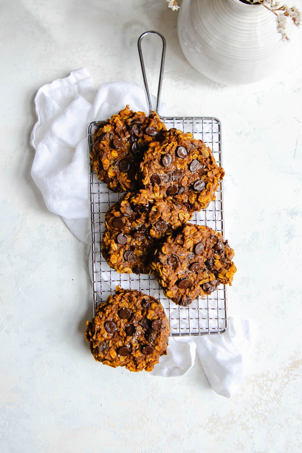 Five pumpkin oatmeal cookies arranged on a small cookie grate over a white linen napkin.