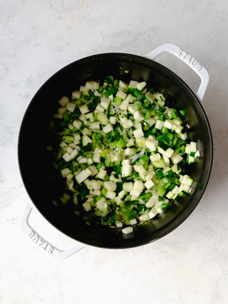 White Staub cast iron pot with sautéed leeks, celery, broccoli and zucchini